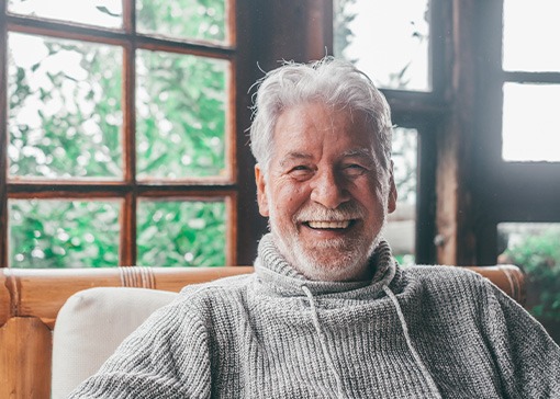 An older smiling and laughing man sitting on a wooden chair