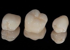 Three dental crowns on dark, reflective surface