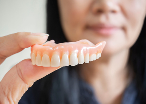 Woman holding upper arch of dentures to the camera