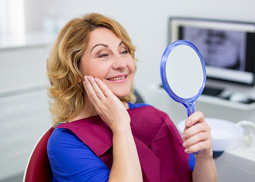 Woman looking at smile after fixed bridge tooth replacement