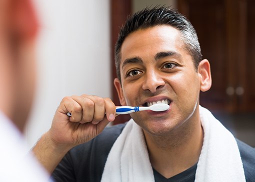 Man caring for his fixed bridge by brushing his teeth