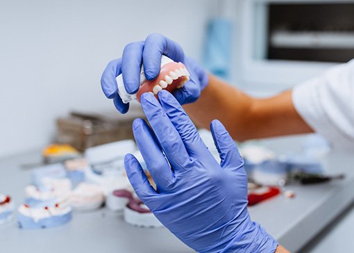 Gloved hands holding a removable denture