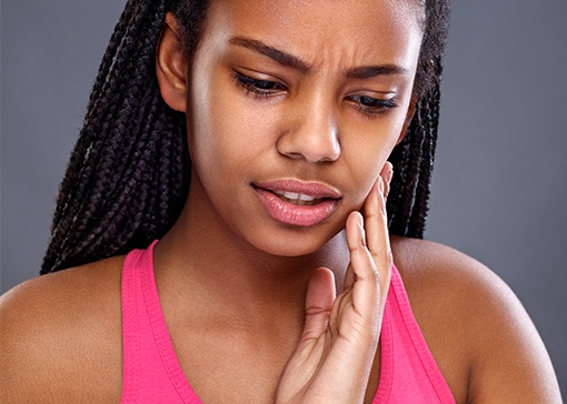 Woman in pain holding cheek before emergency dentistry