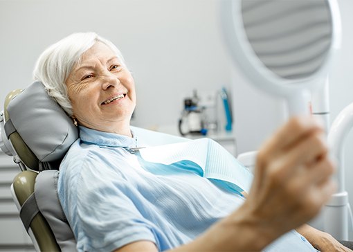 Woman looking at smile after dental implant supported denture placement