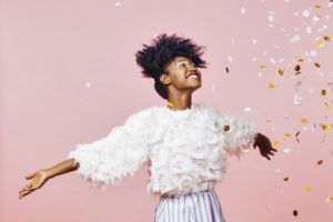 young woman smiling with confetti against light pink background 